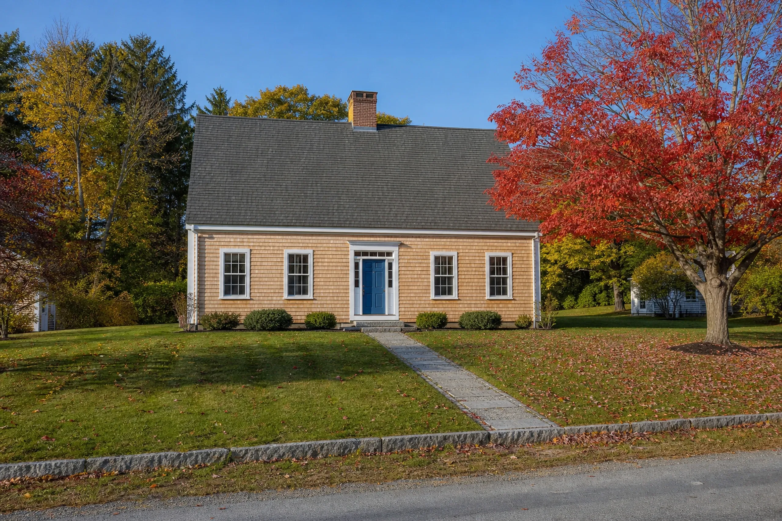 Freeport re-sided village cape in October: a re-sided Cape Cod house on a Freeport village lane, natural eastern white cedar shingles with crisp white trim, a paneled blue door and a granite step, a red maple dropping color across the lawn in cool clear October morning light.